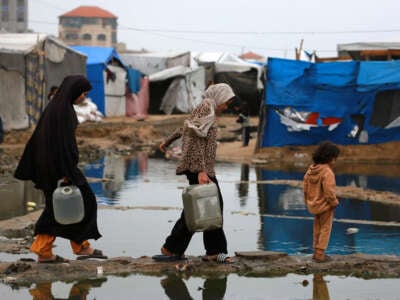 Displaced Palestinians use a dry path to carry water to their tent, following heavy rainfall north of Deir el-Balah in the central Gaza Strip on November 24, 2024.