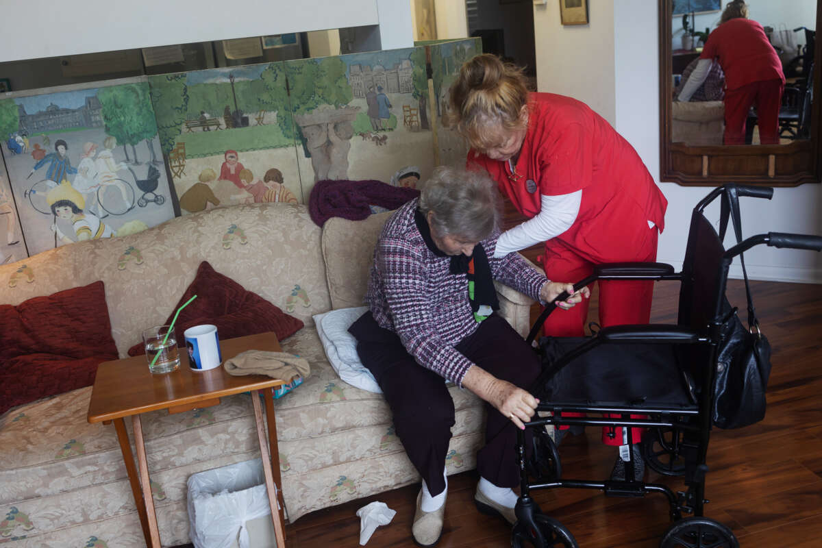 An elderly woman is helped up by a home care worker