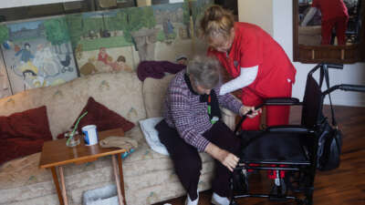 An elderly woman is helped up by a home care worker