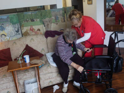 An elderly woman is helped up by a home care worker