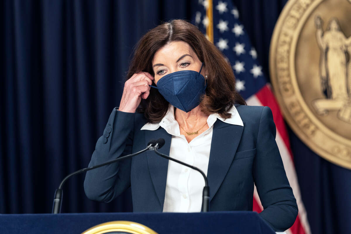 Kathy Hochul begins to remove a medical mask that she is wearing