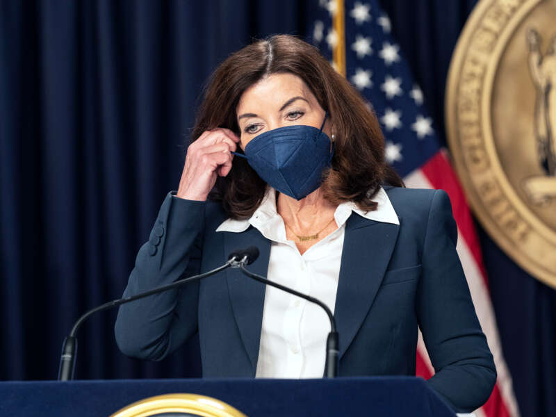 Kathy Hochul begins to remove a medical mask that she is wearing