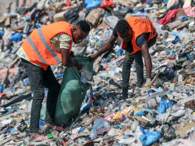 Two men in orange vests clean a beach covered in garbage