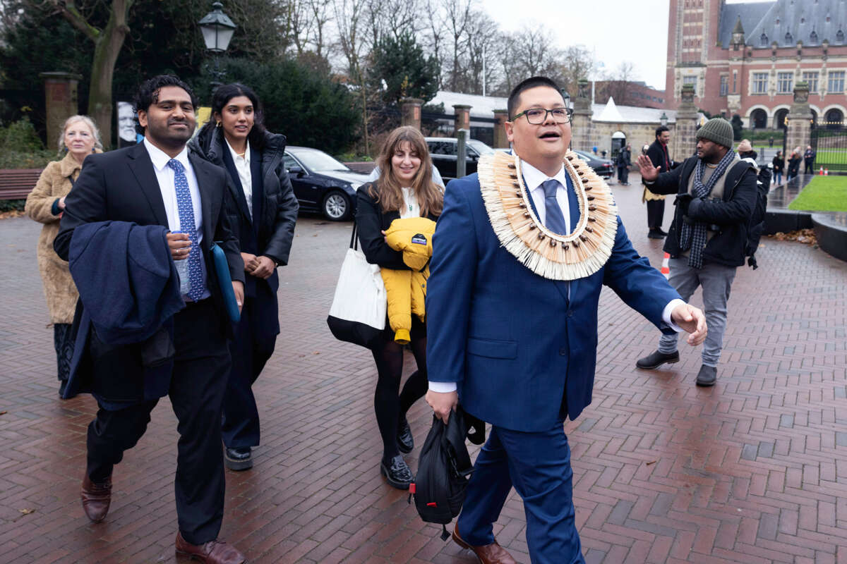 A man in a western suit adorned with traditional regalia walks with others