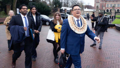 A man in a western suit adorned with traditional regalia walks with others