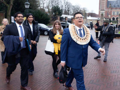 A man in a western suit adorned with traditional regalia walks with others