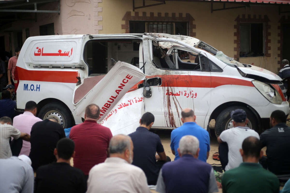 Palestinians sit on the ground close to a damaged ambulance as they take part in Friday Noon prayers in the driveway of the emergency entrance of the Nasser Hospital in Khan Younis, in the southern Gaza Strip on October 27, 2023.