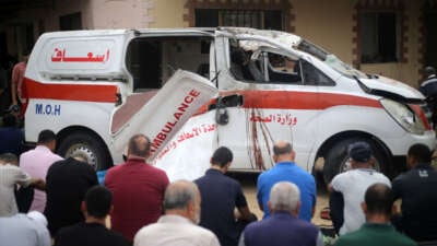 Palestinians sit on the ground close to a damaged ambulance as they take part in Friday Noon prayers in the driveway of the emergency entrance of the Nasser Hospital in Khan Younis, in the southern Gaza Strip on October 27, 2023.