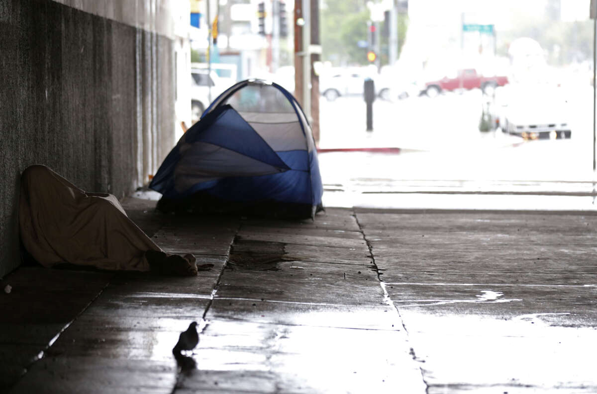 A homeless man huddles under a blanket and out of the rain beneath the 405 Freeway in Los Angeles, California, on January 5, 2016.