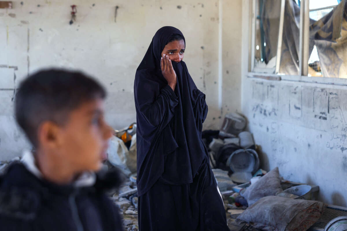 A young woman in a black jilbab weeps as she stands amid rubble