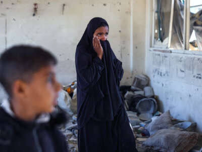 A young woman in a black jilbab weeps as she stands amid rubble