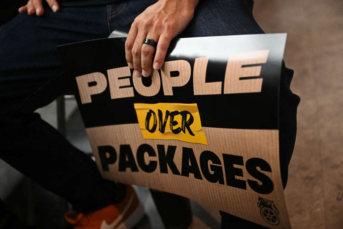 An attendee holds a People Over Packages sign during a rally with workers and union members as part of an Amazon Teamsters Day of Solidarity in support of the unionization and collective bargaining of Amazon delivery drivers at the Teamsters Local 848 on August 29, 2024, in Long Beach, California.