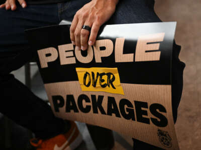 An attendee holds a People Over Packages sign during a rally with workers and union members as part of an Amazon Teamsters Day of Solidarity in support of the unionization and collective bargaining of Amazon delivery drivers at the Teamsters Local 848 on August 29, 2024, in Long Beach, California.