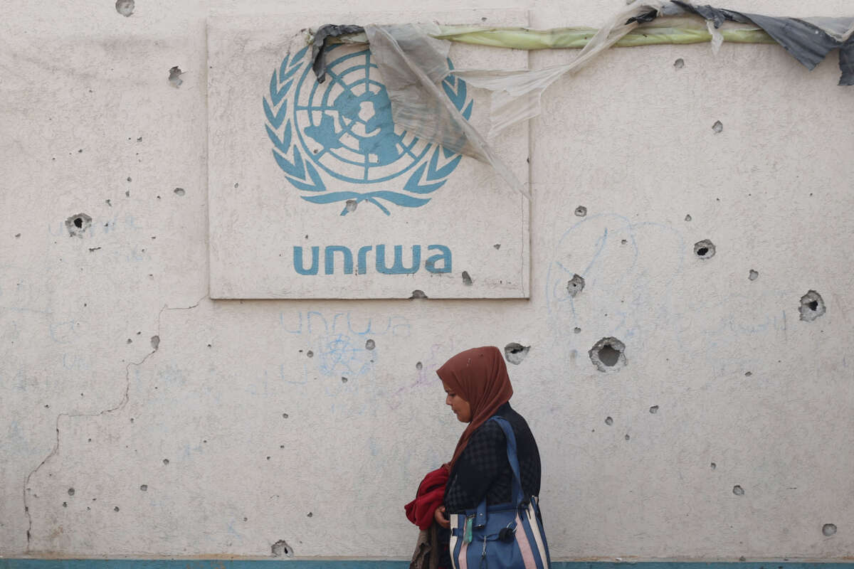 A Palestinian woman walks past a damaged wall bearing the UNRWA logo at a camp for internally displaced people in Rafah in the southern Gaza Strip on May 28, 2024.