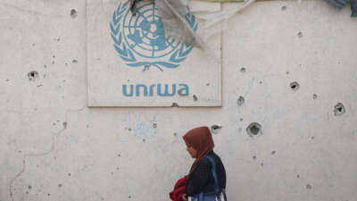 A Palestinian woman walks past a damaged wall bearing the UNRWA logo at a camp for internally displaced people in Rafah in the southern Gaza Strip on May 28, 2024.