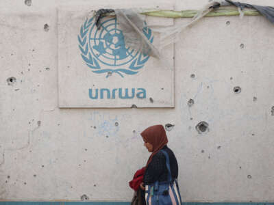 A Palestinian woman walks past a damaged wall bearing the UNRWA logo at a camp for internally displaced people in Rafah in the southern Gaza Strip on May 28, 2024.