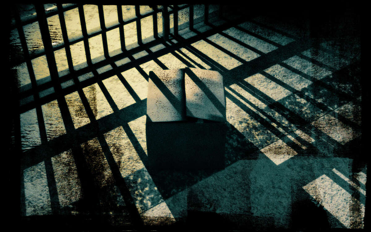 A cardboard box sits in front of a cell with shadows of prison bars cast over it