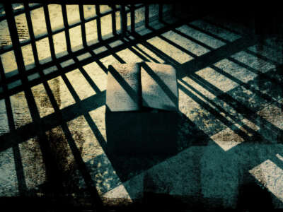 A cardboard box sits in front of a cell with shadows of prison bars cast over it