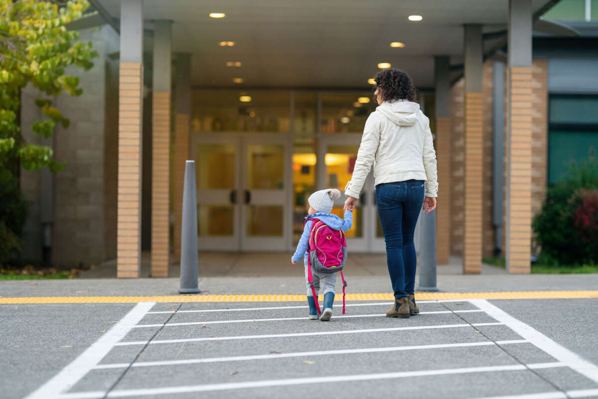 Mother and child walk hand in hand toward building