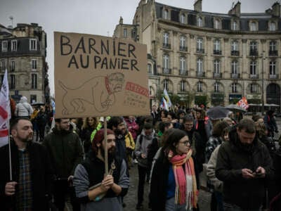 A protester holds a placard reading "Barnier in the basket, watch out homophobic and racist dog" as he marches at a demonstration during a strike called by French unions to open up a social front in the midst of a political crisis, the day after Prime Minister Michel Barnier's government fell on a motion of no-confidence, in Bordeaux, southwestern France, on December 5, 2024.