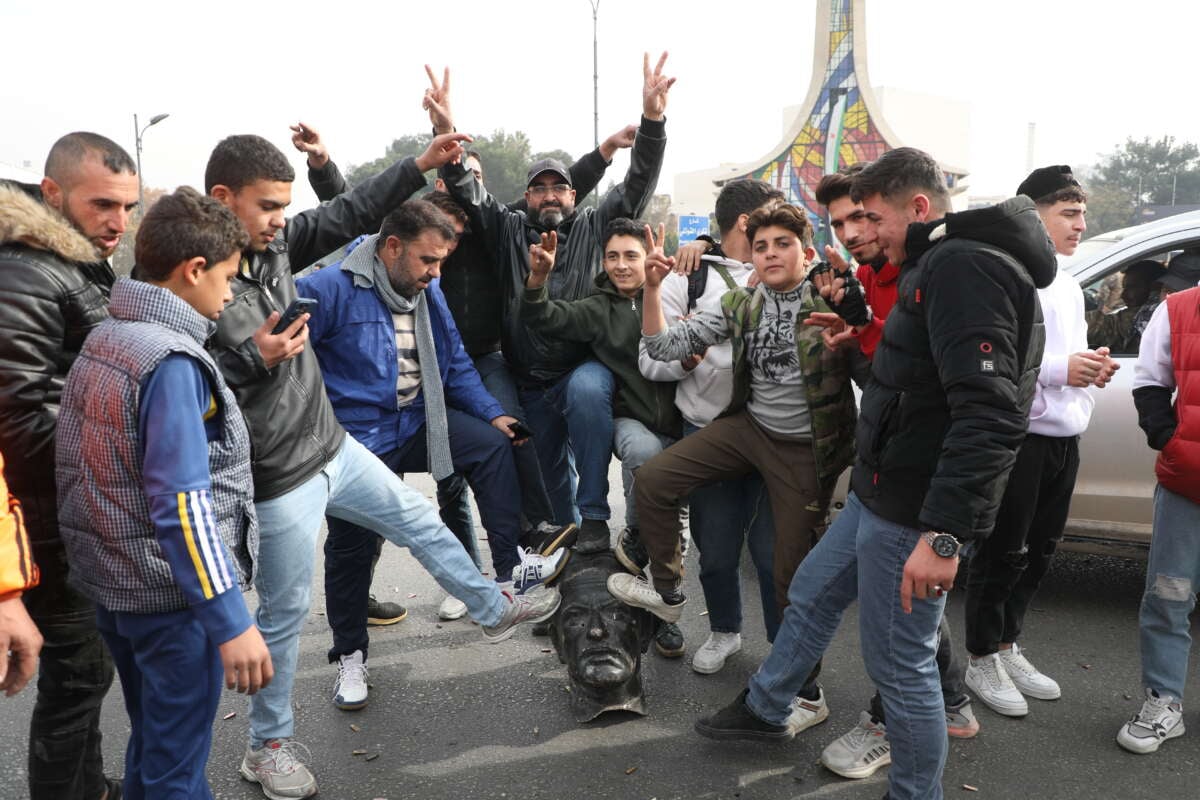 Syrians pose with a vandalized statue of Hafez al-Assad, father of Bashar al-Assad, in Umayyad Square on December 8, 2024, in Damascus, Syria.