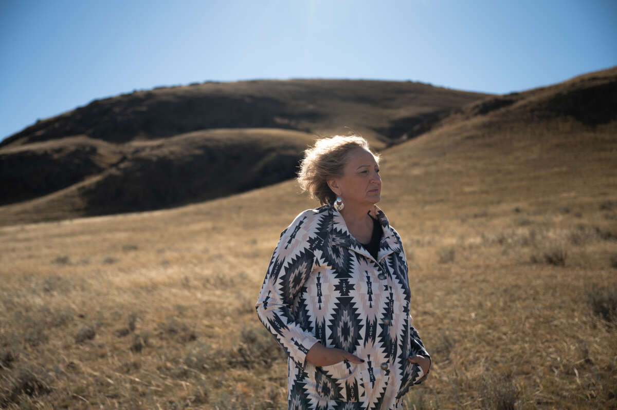 A woman stands on a hilly landscape, the sun highlighting her hair