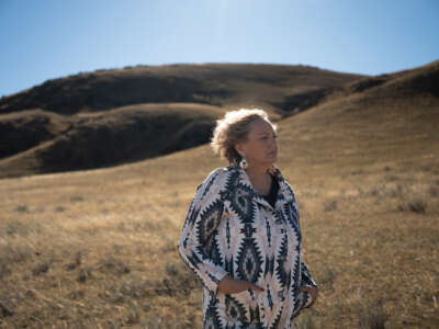 A woman stands on a hilly landscape, the sun highlighting her hair