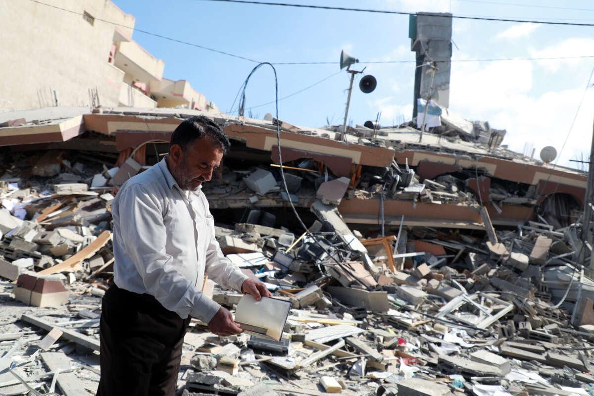 A man looks into a book he's holding as he stands beside the rubble of a building