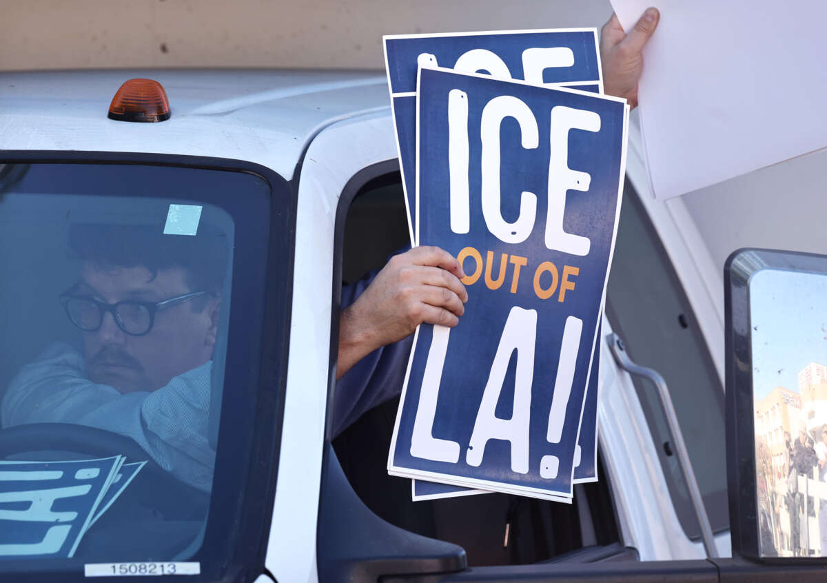 A person holds signs out of their car window reading "ICE OUT OF LA"