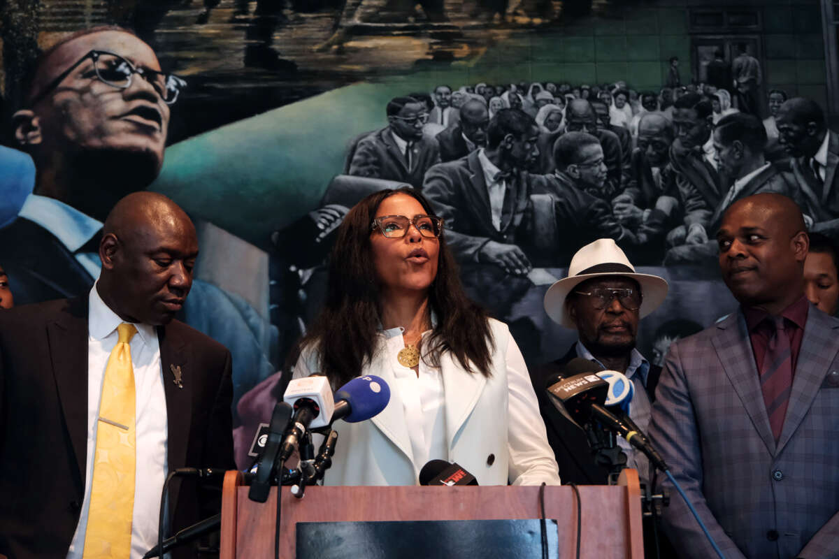 IIyasah Shabazz speaks in front of a mural depicting her late father, Malcolm X, as she stands beside others