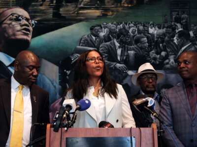 IIyasah Shabazz speaks in front of a mural depicting her late father, Malcolm X, as she stands beside others