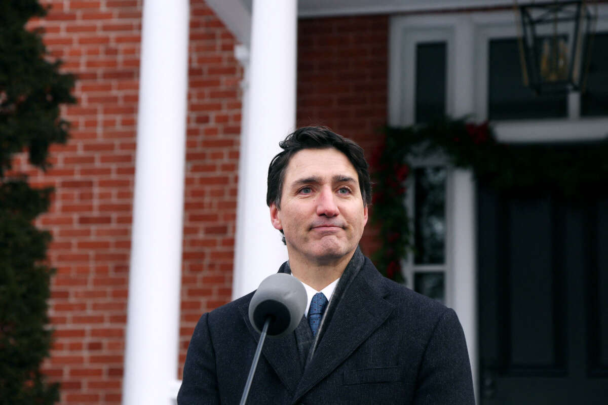 Justin Trudeau stands in front of a brick house and makes an expression that isn't quite smiling