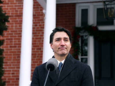 Justin Trudeau stands in front of a brick house and makes an expression that isn't quite smiling