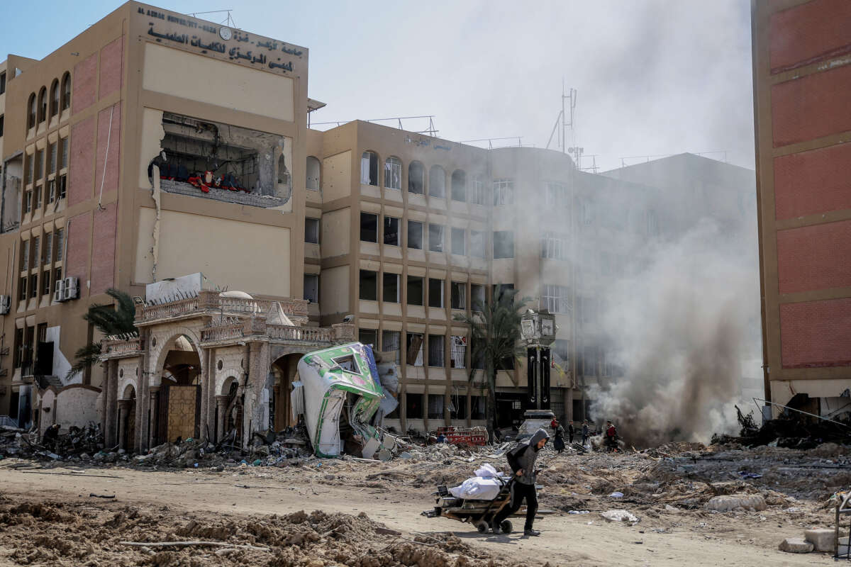 A young Palestinian pulls a wheel cart past the heavily damaged building of Al Azhar University in Gaza City on February 15, 2024.