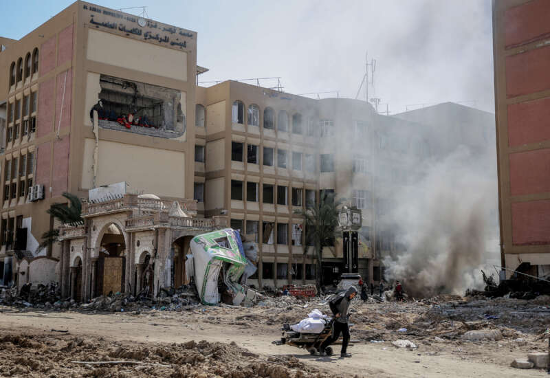 A young Palestinian pulls a wheel cart past the heavily damaged building of Al Azhar University in Gaza City on February 15, 2024.