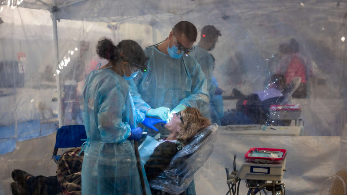 Two dentists in full ppe work on the mouth of a patient in a remote clinic