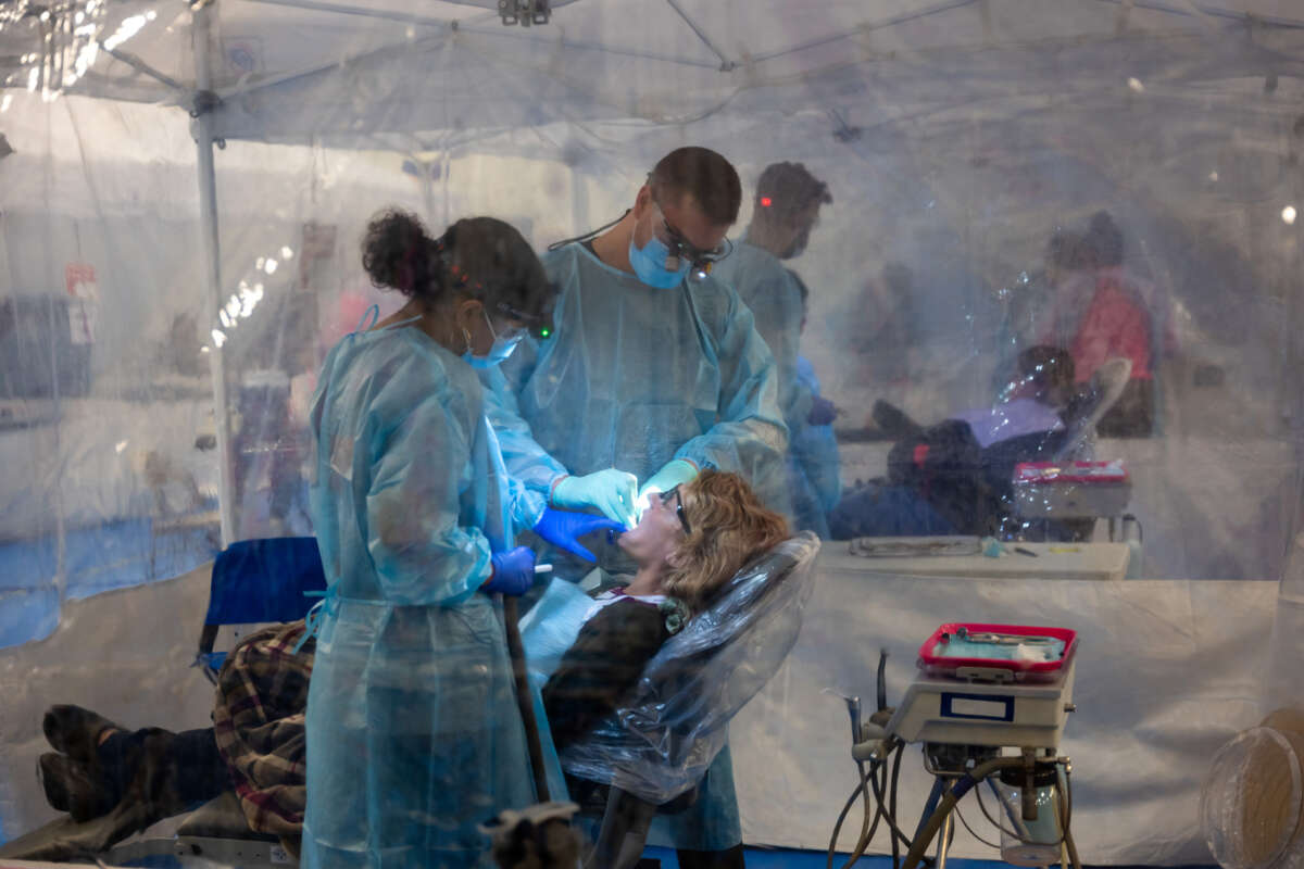 Two dentists in full ppe work on the mouth of a patient in a remote clinic