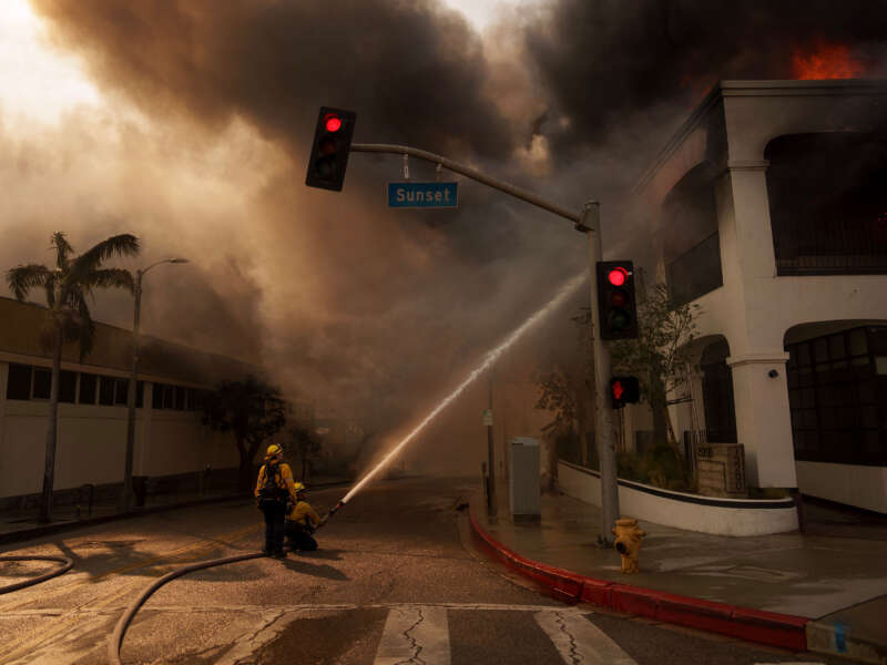 Firefighters spray flames from the Palisades Fire burning a business on January 8, 2025, in the Pacific Palisades neighborhood of Los Angeles, California.