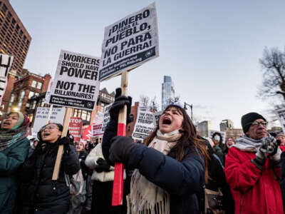 People in winter wear hold signs reading "WORKERS SHOULD HOLD THE POWER, NOT BILLIONAIRES" in English and Spanish during an outdoor demonstration