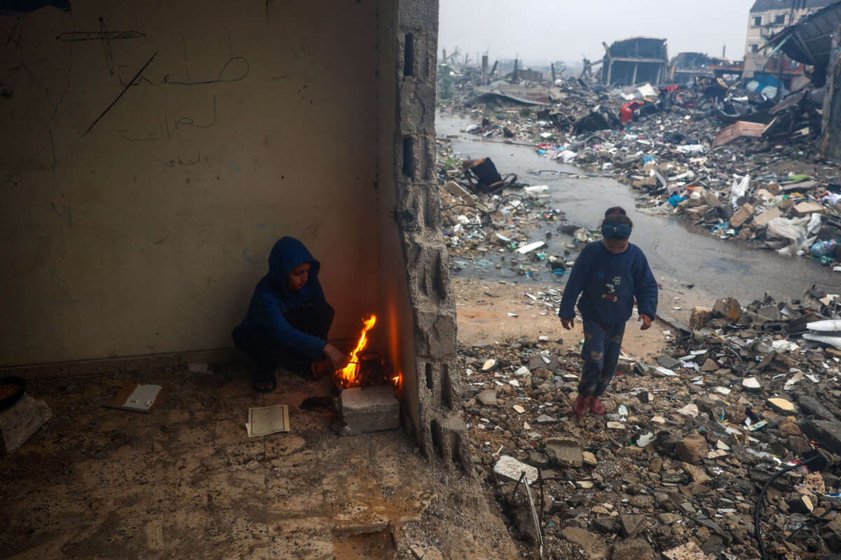 Palestinian children light a fire to warm up in a damaged building amidst rubble on a rainy day in Bureij in the central Gaza Strip on January 23, 2025, days into a ceasefire deal in the war between Israel and the Palestinian Hamas movement.