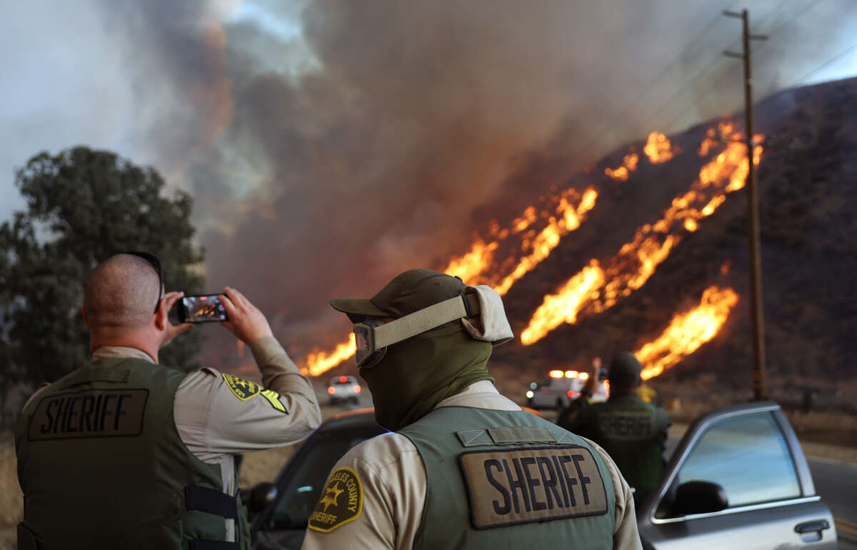 Sheriffs stand on the side of the road and photograph the fire on their phones