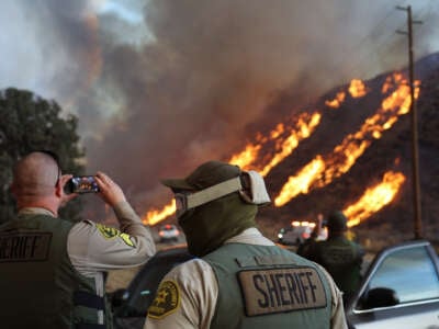 Sheriffs stand on the side of the road and photograph the fire on their phones