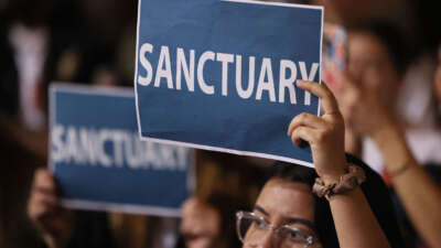 People in the audience hold up signs as the Los Angeles City Council considers a 'sanctuary city' ordinance at City Hall in Los Angeles, California, on November 19, 2024.