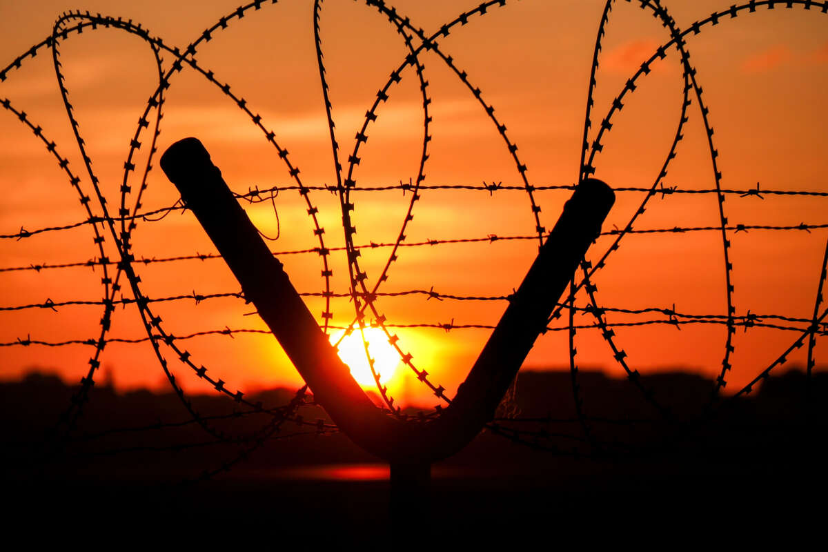 Barbed wire and razor wire fence with sun setting