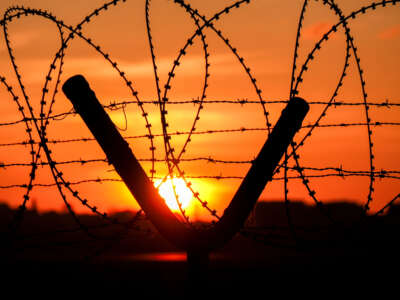 Barbed wire and razor wire fence with sun setting