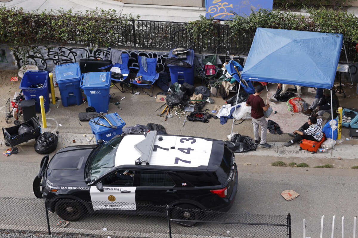 A San Diego police office drives by unhoused people gathered in an encampment on November 18, 2024, in San Diego, California.