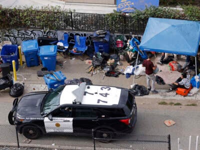 A San Diego police office drives by unhoused people gathered in an encampment on November 18, 2024, in San Diego, California.