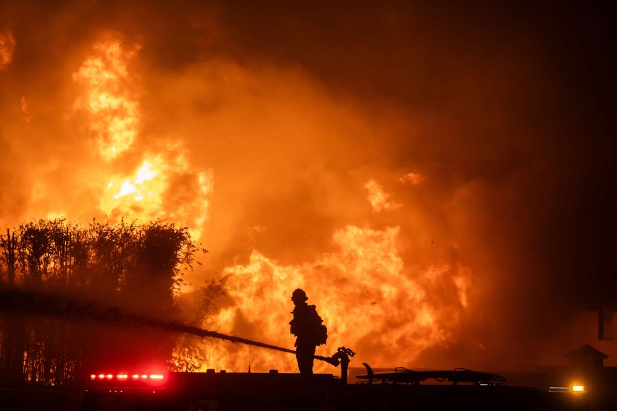 A firefighter stands on top of a fire truck to battle the Palisades Fire while it burns homes on the Pacific Coast Highway amid a powerful windstorm on January 8, 2025, in Los Angeles, California.