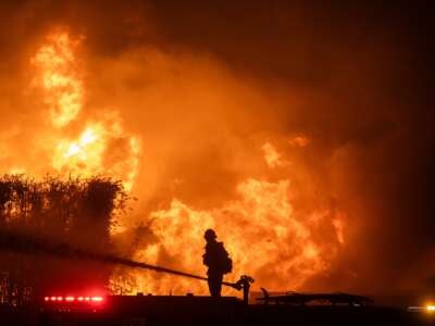 A firefighter stands on top of a fire truck to battle the Palisades Fire while it burns homes on the Pacific Coast Highway amid a powerful windstorm on January 8, 2025, in Los Angeles, California.