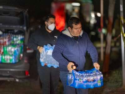 Volunteers bring water to give to people who remained in a few of the houses left among the thousands that burned the Eaton Fire, on January 12, 2025, in Altadena, California. Water is an important commodity as the tap water system was contaminated with the chemical toxins of thousands of burned structures.